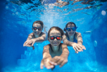Three children swimming in a pool with goggles on.